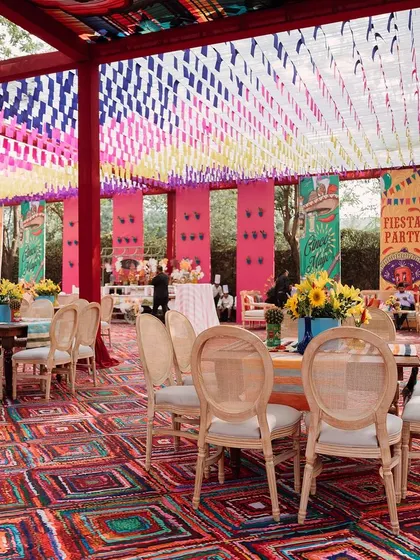 A wide view of the dining area, with its colorful woven ceiling and vibrant rug. The space is designed to be open and airy, perfect for a daytime celebration.