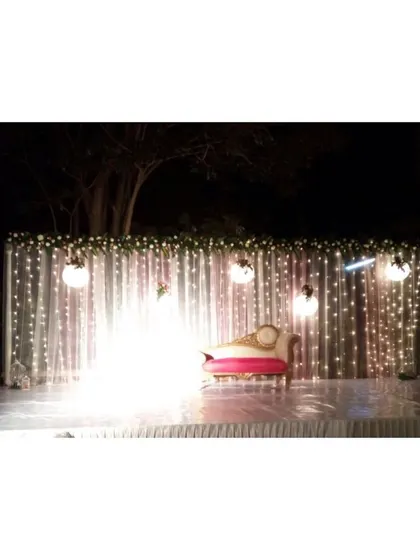 A minimalist night reception stage set against a dark backdrop. The curtain of fairy lights and hanging orb lights creates a simple, starry effect, focusing all the attention on the couple's seating.