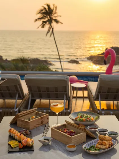 A breathtaking sunset shot of a full meal spread by an infinity pool, capturing the ultimate luxury dining experience in Goa.