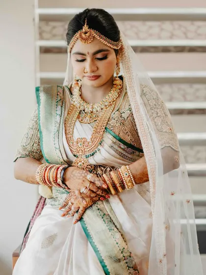A moment of quiet grace. Our bride looks down, showing off the stunning detail of her hand-embroidered blouse and the beautiful drape of her silk saree, complete with a sheer veil.