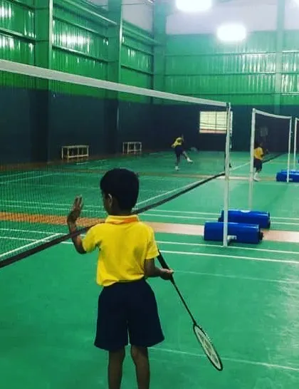 A young player practices his stance at the net, ready to return a shot. Focusing on these fundamental skills helps build a solid foundation for future badminton success.