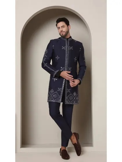 The 'Neel Amber' achkan in a rich navy blue. This full-length shot displays the geometric and mirrored embellishments that run down the placket and hem, offering a modern take on royal attire.