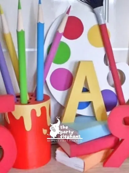 Custom props for the art party included these oversized foam models of a pencil holder, paint palette, and the birthday girl's initial, adding a playful and thematic touch to the decor.