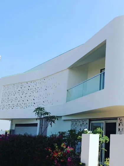 A detail of a residence featuring a seamless, curved white wall with a perforated screen. The leaf-like perforations create intricate light patterns while providing ventilation and privacy.