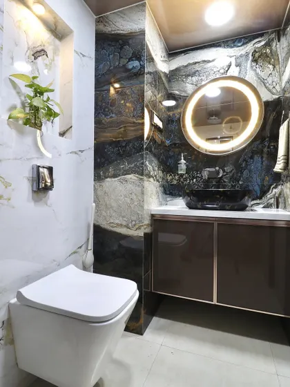 A full view of the bathroom, showing the toilet and the vanity area. The design uses contrasting marble tiles to create distinct zones, with the backlit mirror adding a warm glow.
