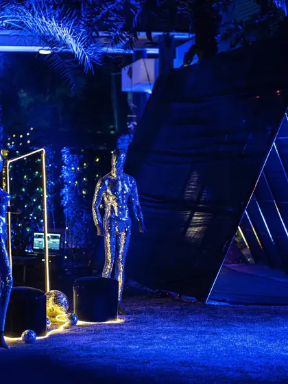 A futuristic party setup with shimmering silver mannequins and a dramatic triangular entrance, all bathed in electric blue light for a high-impact look.