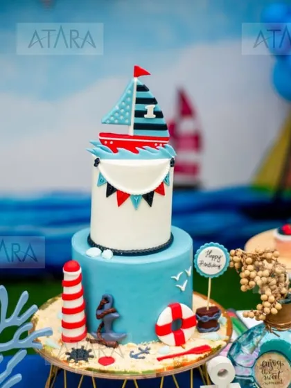 A beautifully crafted cake for a nautical-themed first birthday. The cake features a sailboat, a lighthouse, an anchor, and other sea-inspired elements, making it a stunning centerpiece.