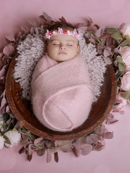 A classic posed newborn session featuring a baby girl swaddled in pink and surrounded by delicate flowers. This highlights our skill in creating elegant, floral-themed portraits in our comfortable studio.