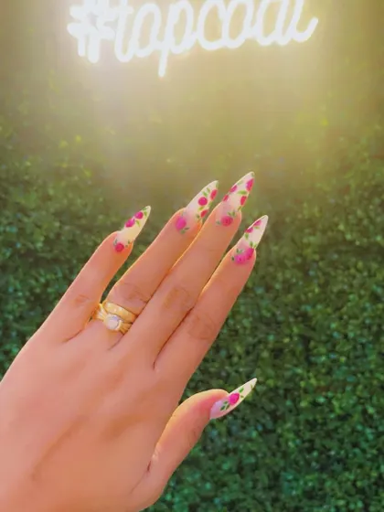 Turning nails into masterpieces is my passion. This photo, taken against our salon's backdrop, showcases a beautiful hand-painted floral design on sharp stiletto nails.