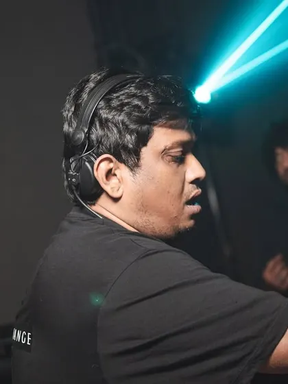 A candid shot from the side, with a laser cutting through the darkness. This captures the focused, intense environment of the DJ booth during a live set.