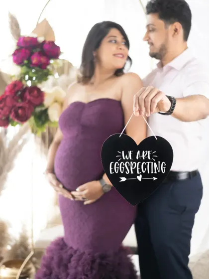 A sweet and funny announcement. The couple holds a heart-shaped sign that reads "We are egg-specting" in this lovely, light-filled studio shot.