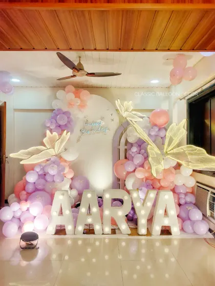 We can transform any space for a magical celebration. This butterfly-themed first birthday features pastel balloons, large lighted marquee letters spelling the name 'AARYA', and beautiful butterfly accents.