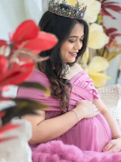 A soft and gentle portrait. The mom-to-be is framed by red flowers in our studio, wearing a lovely pink gown and a crown, capturing a moment of quiet joy.