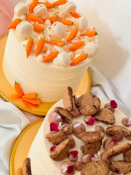 A duo of delicious cakes. One is a carrot cake topped with mini macarons and fondant carrots, and the other is a cookie-topped cake.
