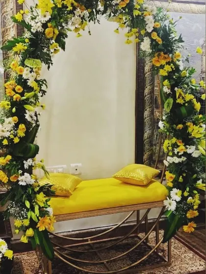 A simple yet elegant seating arrangement for a Haldi or Mehendi ceremony. The yellow bench is framed by a beautiful arch of yellow and white flowers, creating a perfect photo spot.
