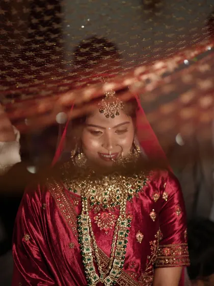 A shy smile from under the veil. This artistic shot captures the timeless beauty of a bride on her wedding day, with her intricate jewelry and soft, glowing makeup.