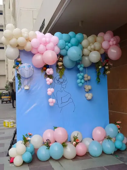 A 'He or She?' themed baby shower with a simple and elegant design. The blue backdrop is adorned with a pink, blue, and white balloon garland.