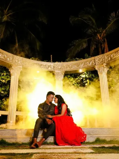 A dramatic night shot with a couple seated in front of a grand, columned structure, surrounded by golden smoke. This creates a mystical and opulent feel.