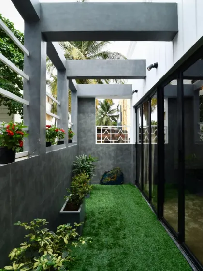 A narrow side courtyard is transformed into a green corridor with artificial turf and potted plants. The design uses vertical space and contrasting textures of concrete and greenery to make the most of a compact area.