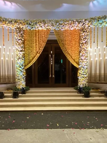 The same marigold entrance transformed for the evening, with warm uplighting and candle-like fixtures creating a magical and inviting glow.