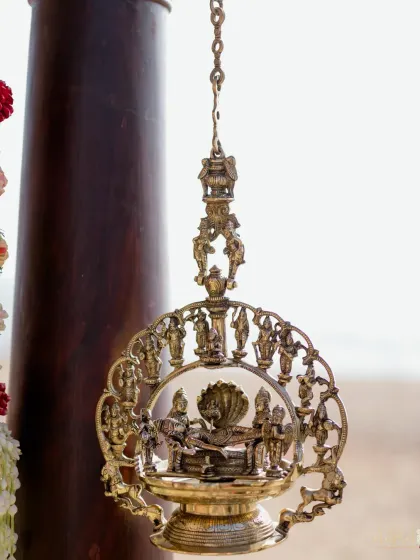 An intricately carved brass lamp, a classic element of South Indian decor, hangs at a sunrise wedding. These details add a touch of divinity and timeless elegance to the celebration.