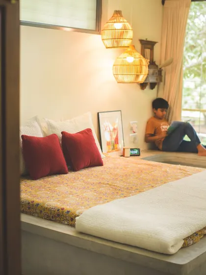 A cozy corner in one of the bedrooms, where a built-in cement bed is adorned with soft textiles. The woven pendant lights and a low window seat create a relaxed, informal atmosphere perfect for unwinding.