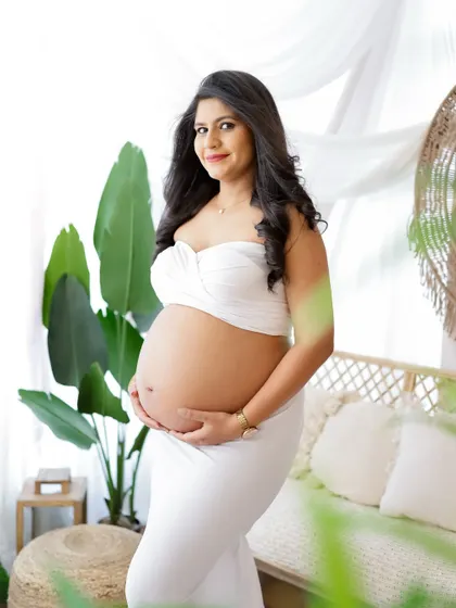 A confident and beautiful portrait in a boho setting. The mom-to-be's white two-piece outfit proudly showcases her baby bump.