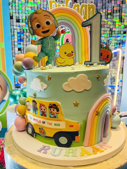 A close-up of the Cocomelon cake, showing the details of the bus, the rainbow, and the cute character toppers.