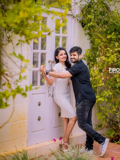 A happy, dancing pose in front of a white door. The couple's casual outfits and their joyful interaction make this a very sweet and candid shot.