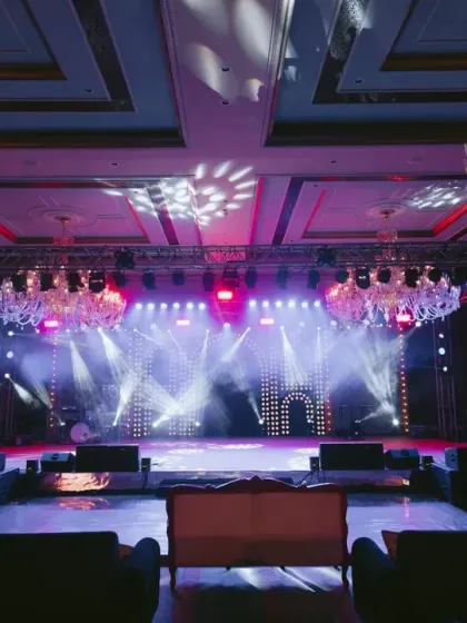 A grand ballroom transformed for a Bollywood-themed Sangeet. The space is dominated by a massive stage and brilliant chandeliers, setting the scene for a night of dazzling performances.