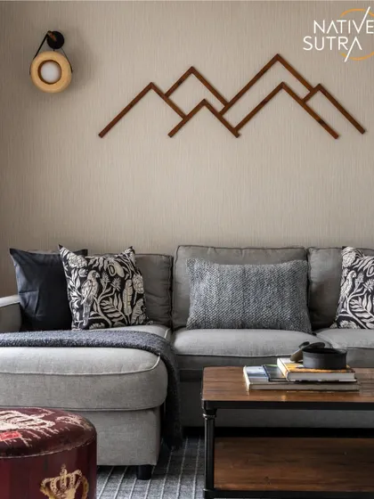 Grounded comfort in a modern minimalist sitting area. The geometric mountain wall art serves as a focal point above the plush grey sofa, while patterned cushions and a leather pouf add layers of texture and personality.