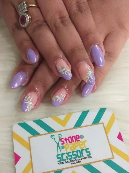 A lovely combination of solid lavender nails and accent nails with a delicate, hand-painted white leaf design over a nude base. This is a soft and elegant nail art option.