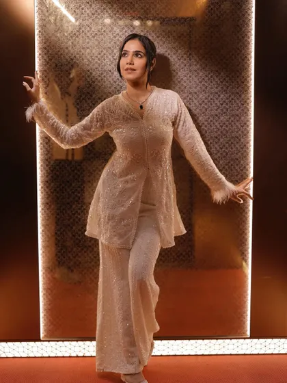 A confident pose in the same white outfit, highlighting the feather details on the sleeves.
