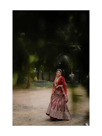 A wide shot of the bride in her red lehenga, standing in a beautiful garden, looking like royalty.
