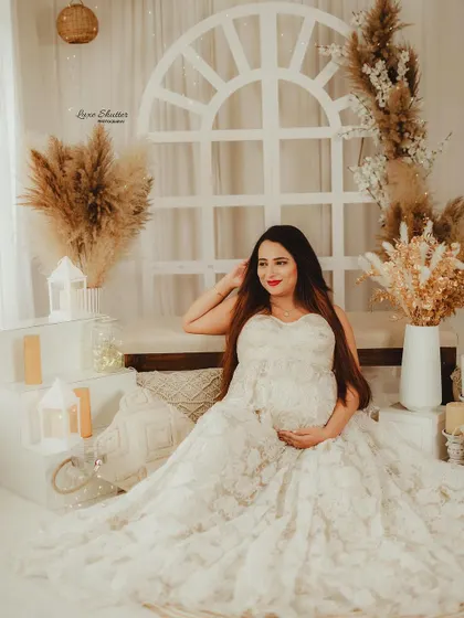 This mom-to-be looks serene and beautiful in her white lace gown, seated in a boho-inspired studio setup.