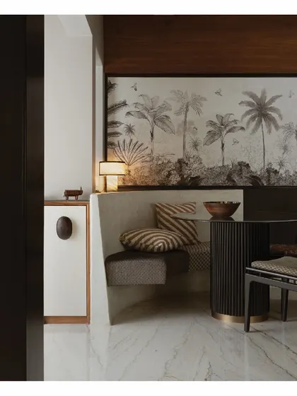 This cozy dining nook features a built-in, arc-shaped bench with custom upholstery. This design choice makes clever use of a corner, providing ample seating without cluttering the space, all set against a beautiful tropical artwork.