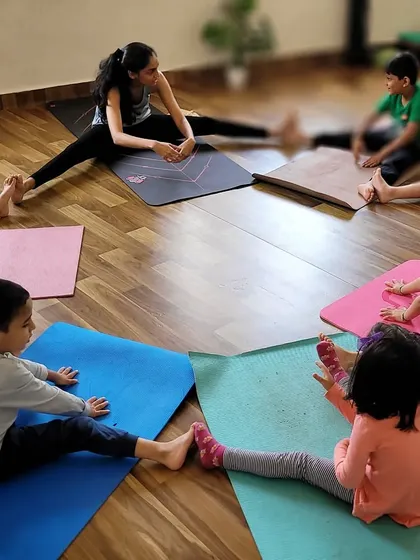 A circle of young yogis stretching together. Group activities like this foster a sense of community and make learning poses like the wide legged forward fold more interactive.