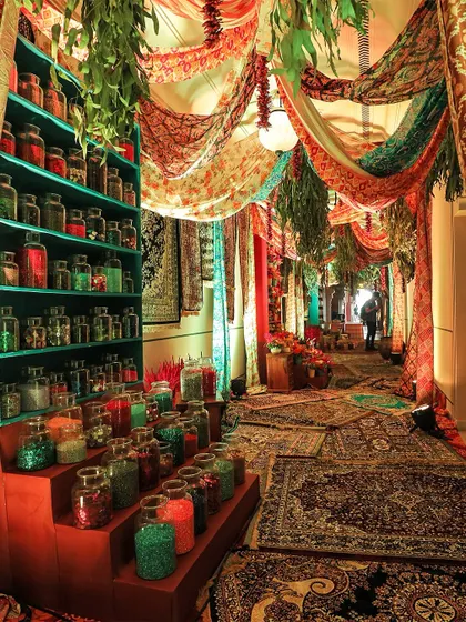 An immersive entrance designed to look like a bustling bazaar, with colorful carpets, draped fabrics, and shelves of spices and glitter, creating a unique and memorable guest experience.