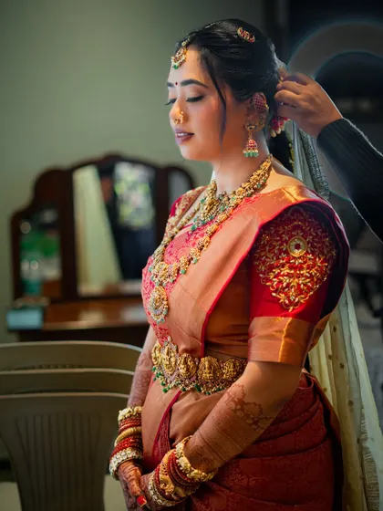A candid moment during the getting-ready process. The makeup is designed to be flawless from every angle, complementing the heavy temple jewellery and rich silk saree.