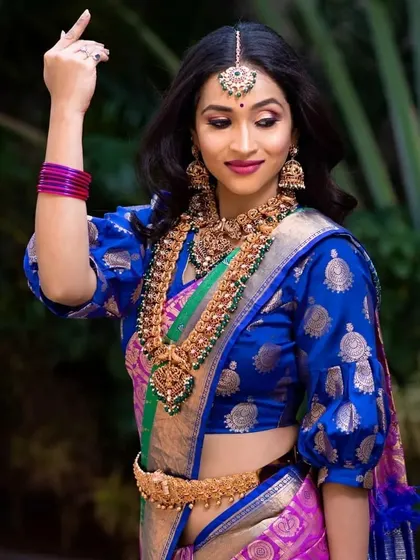 A beautiful shot of a model in a puff-sleeve blouse and silk saree, wearing our multi-layered temple jewellery set.