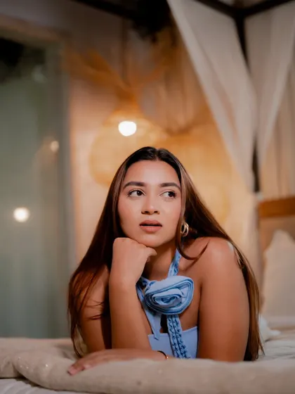 A dreamy indoor portrait of a model lying on a bed. The warm, soft lighting from the lamps creates an intimate and cozy atmosphere.