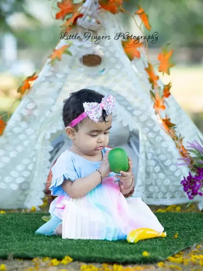 A one-year-old baby girl sits in front of a decorated teepee, curiously examining a toy. These milestone shoots are filled with adorable, exploratory moments.