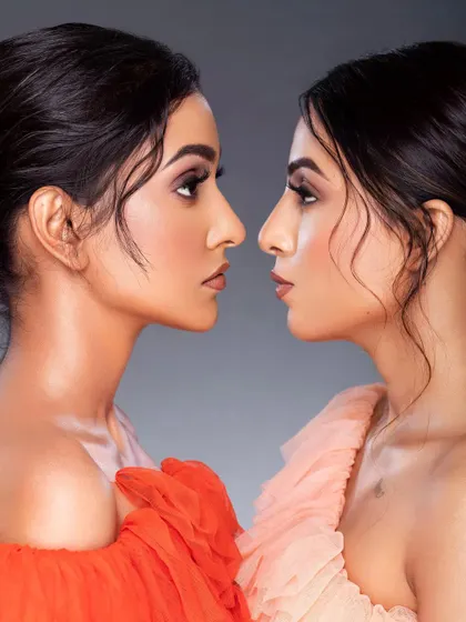 A striking double portrait, creating a mirror-like effect. The composition is artistic and symmetrical, showcasing the models' profiles and the clean, soft-glam makeup.