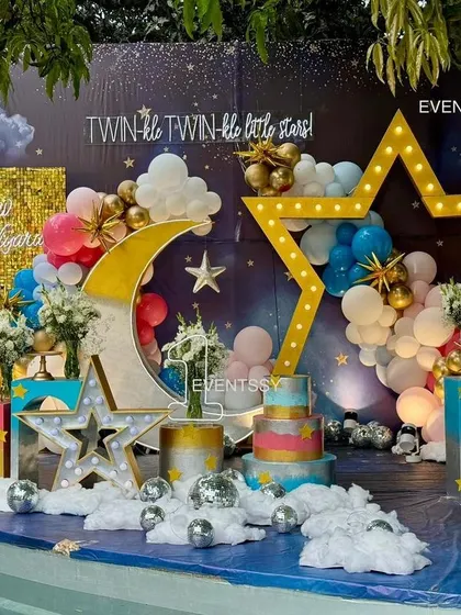 A full view of the "Twinkle Twinkle" stage setup by a pool, with the decor reflecting beautifully on the water. The use of pink and blue balloons makes it perfect for boy-girl twins.