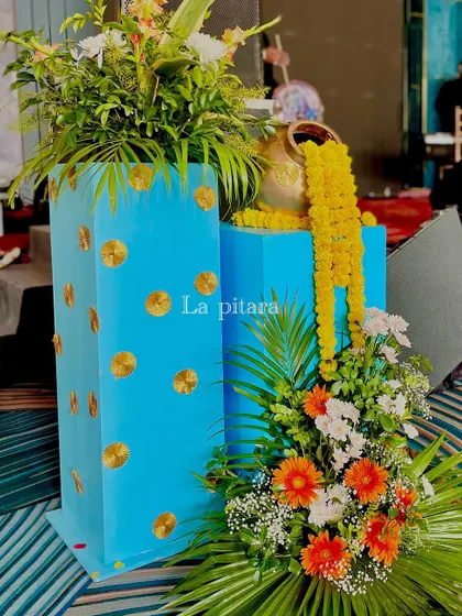A vibrant floral arrangement using bright blue pedestals, with marigold garlands spilling from a golden pot. This added a pop of color and traditional flair to the event space.
