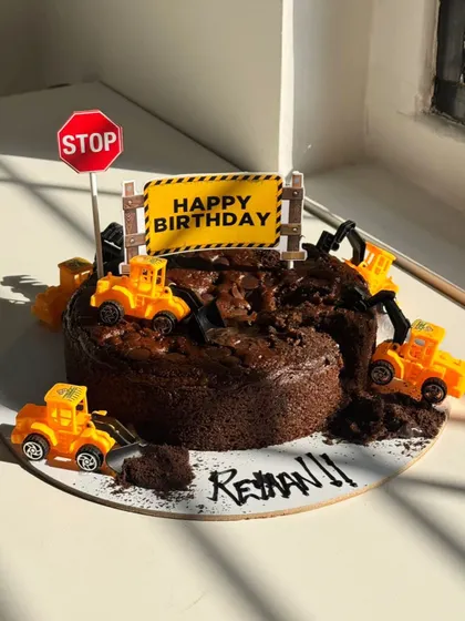 Under construction, but make it delicious! This fun construction-themed cake features toy trucks digging into a rich chocolate cake, perfect for a young builder's birthday.