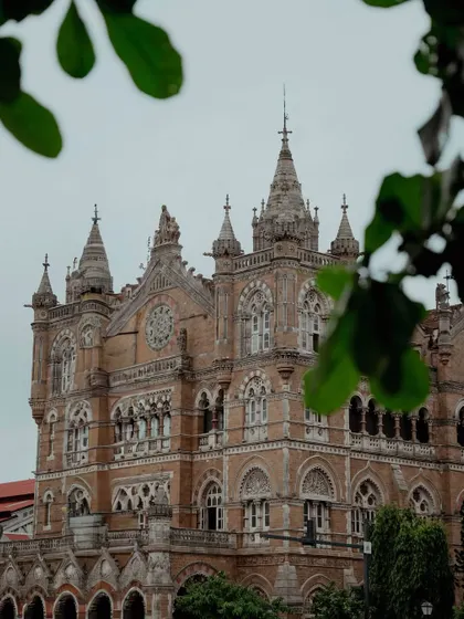 Wide shots of the CSMT building, showcasing its intricate Victorian Gothic design. The presence of the iconic red double-decker buses adds to the vintage charm.