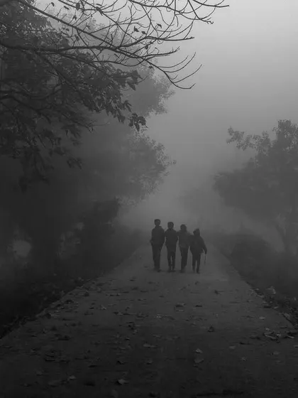 A group of friends walks down a path into the dense fog. This black and white image evokes a sense of mystery, journey, and togetherness.