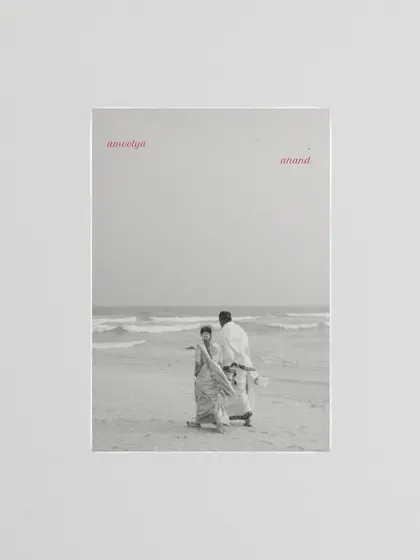 A black and white photo of a couple on the beach, framed with the words 'amoolya anand' (precious joy). This artistic composition turns a simple moment into a poetic statement.