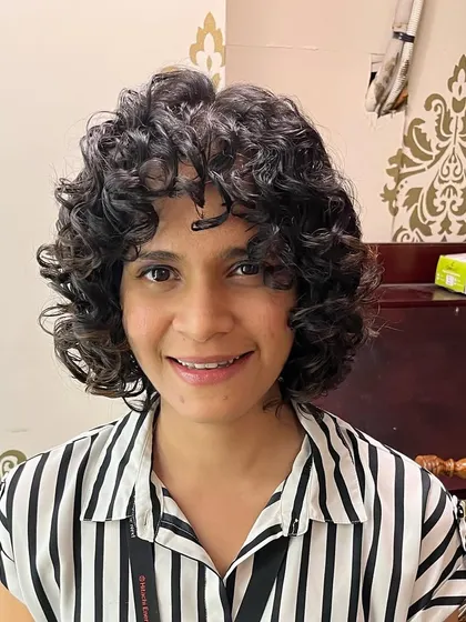 A happy client showing off her new curly bob with bangs. This cut is designed to be wash-and-go.